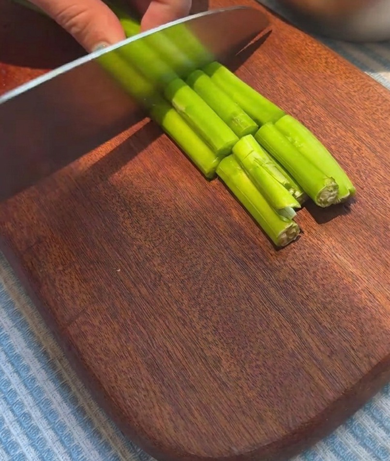 Mazzi di asparagi freschi tagliati in pezzi uniformi su un tagliere di legno.