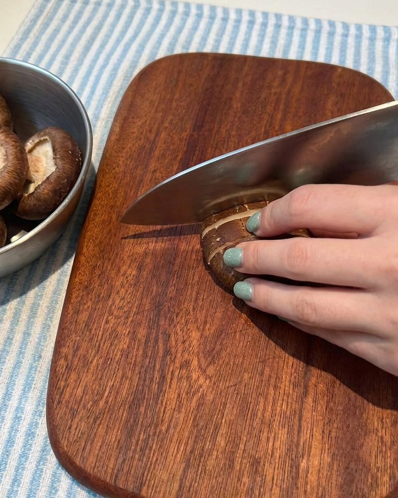 Funghi freschi tagliati accuratamente in fettine sottili su un tagliere di legno.