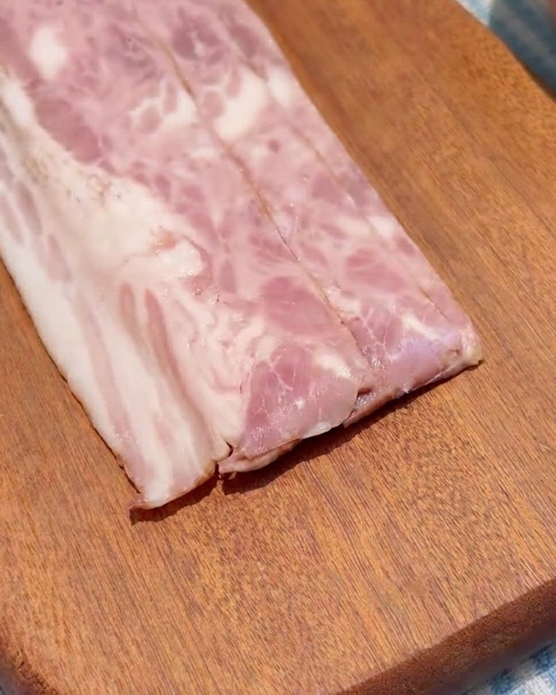 Strisce di pancetta tagliate in cubetti uniformi su un tagliere di legno.
