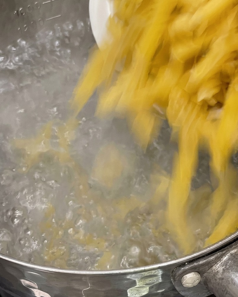 Pasta cruda che viene versata in una pentola di acqua bollente.