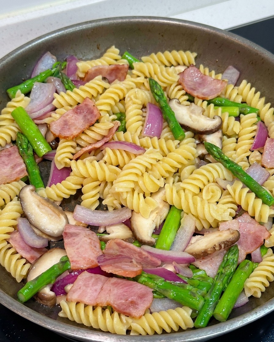 Pasta che si amalgama con verdure e pancetta in padella, condita con pepe nero e salsa di soia.