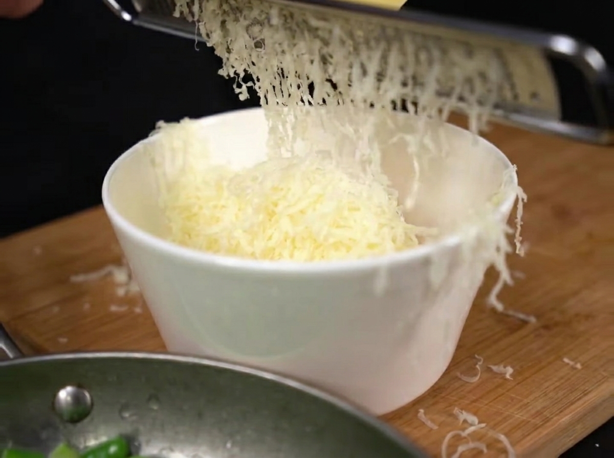 Parmigiano appena grattugiato che cade in un mucchietto sopra i tuorli duovo in una ciotola.