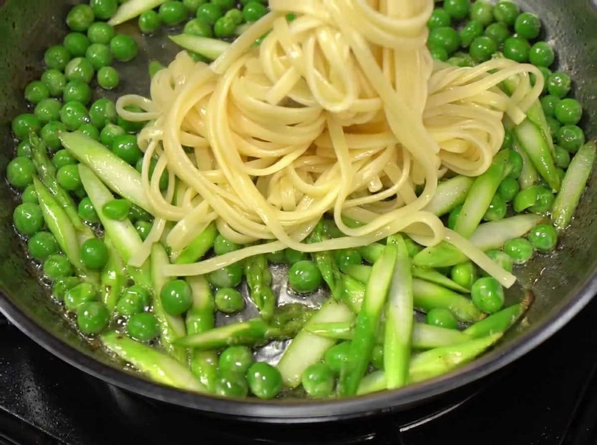 Spaghetti sollevati dallacqua bollente e aggiunti a una padella di verdure saltate e bacon.