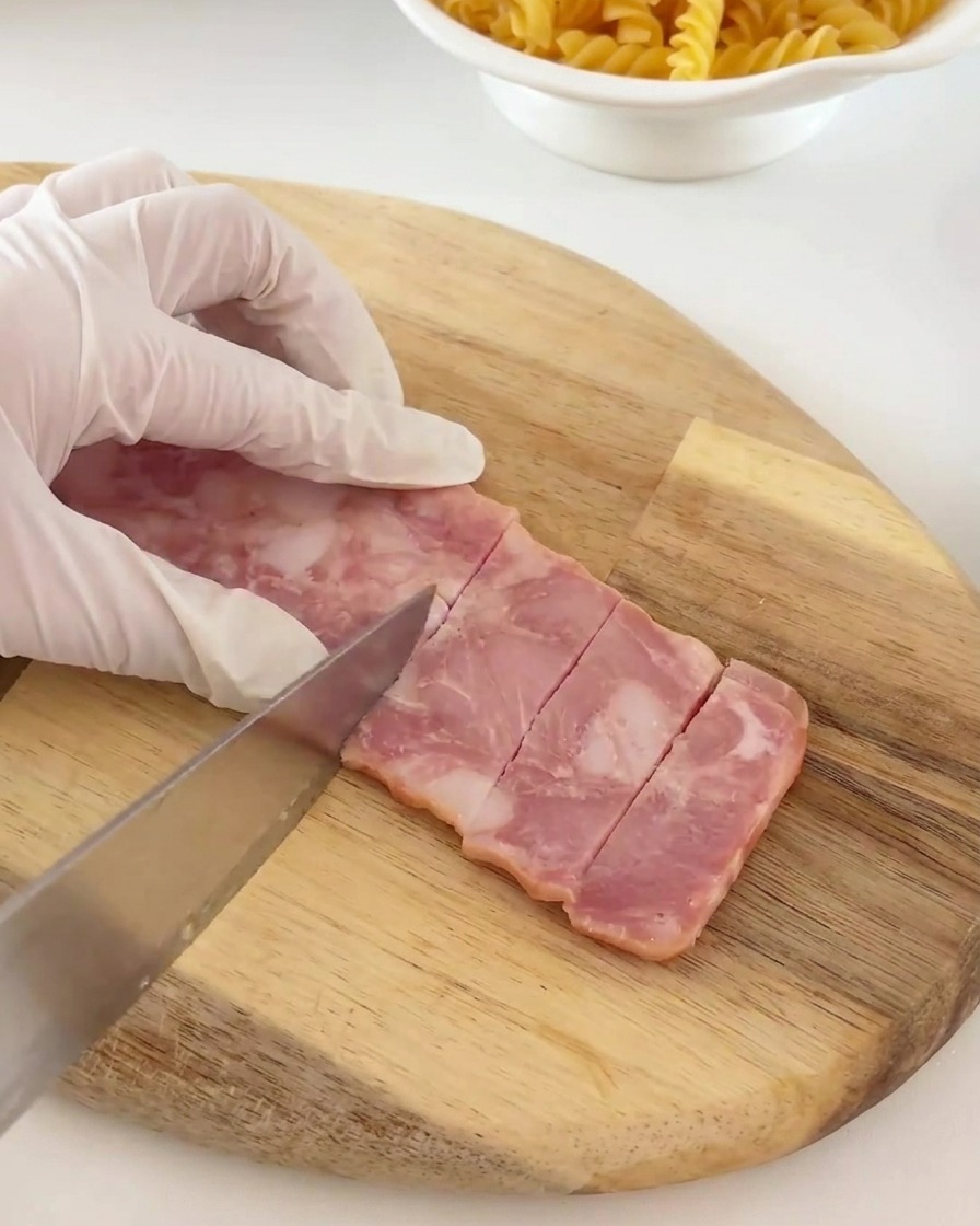 Strisce di pancetta tagliate in piccoli pezzi rettangolari uniformi su un tagliere.