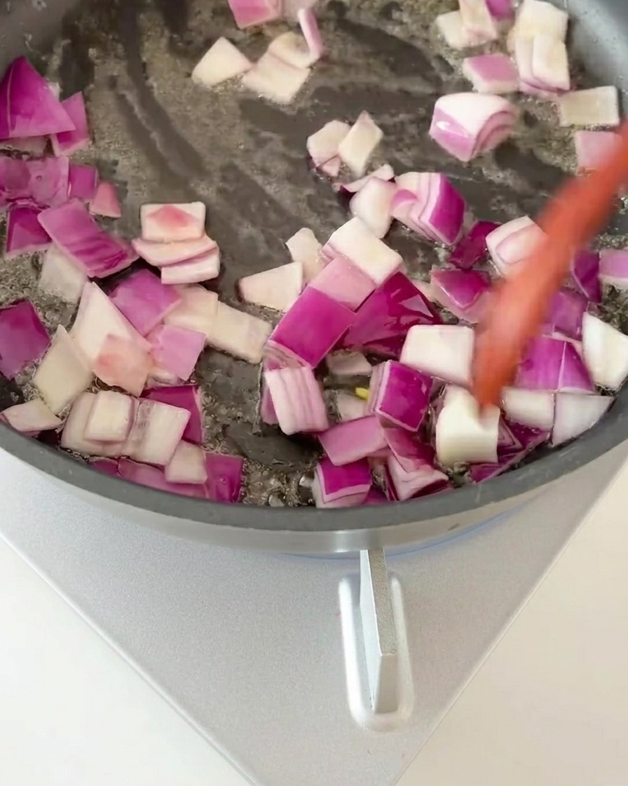 Cubi di cipolla rossa mescolati in una padella calda fino a diventare fragranti.