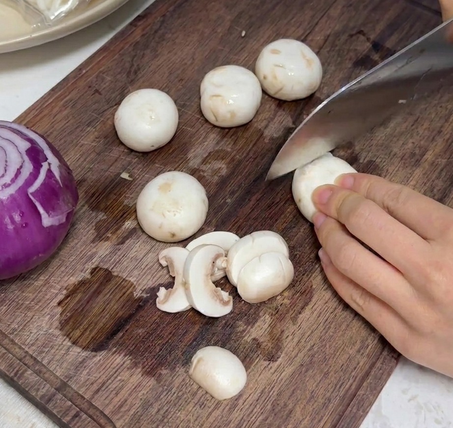 Funghi prataioli freschi tagliati a fettine uniformi su un tagliere di legno.