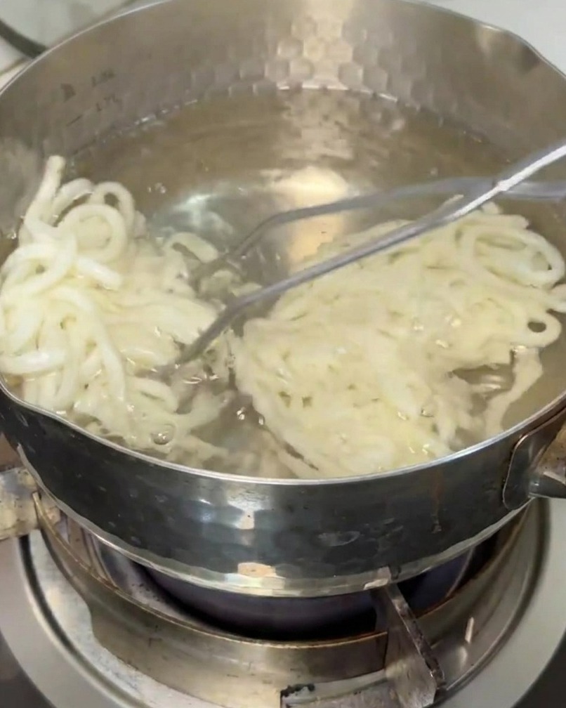 Noodles udon sollevati da una pentola di acqua bollente con una schiumarola.