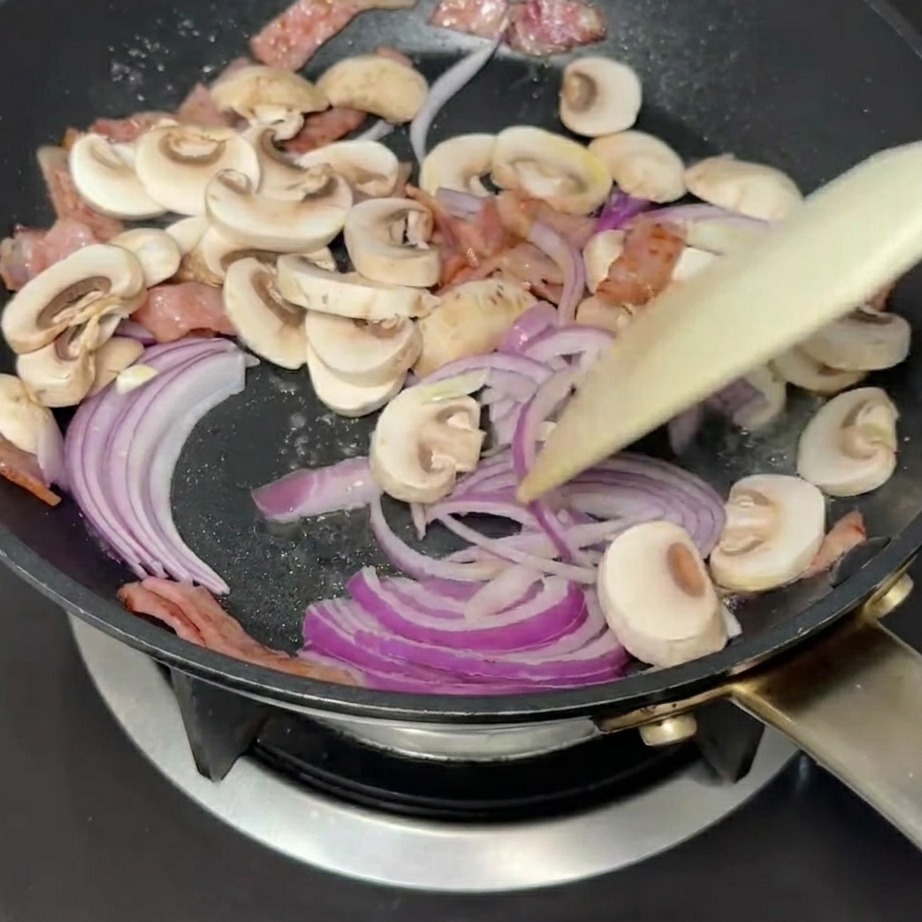 Cipolle rosse e funghi a fette mescolati in padella con la pancetta.