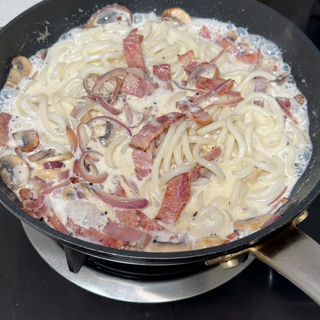 Salsa tartufata nera mescolata in una padella con pancetta croccante, funghi a fette e cipolle caramellate.