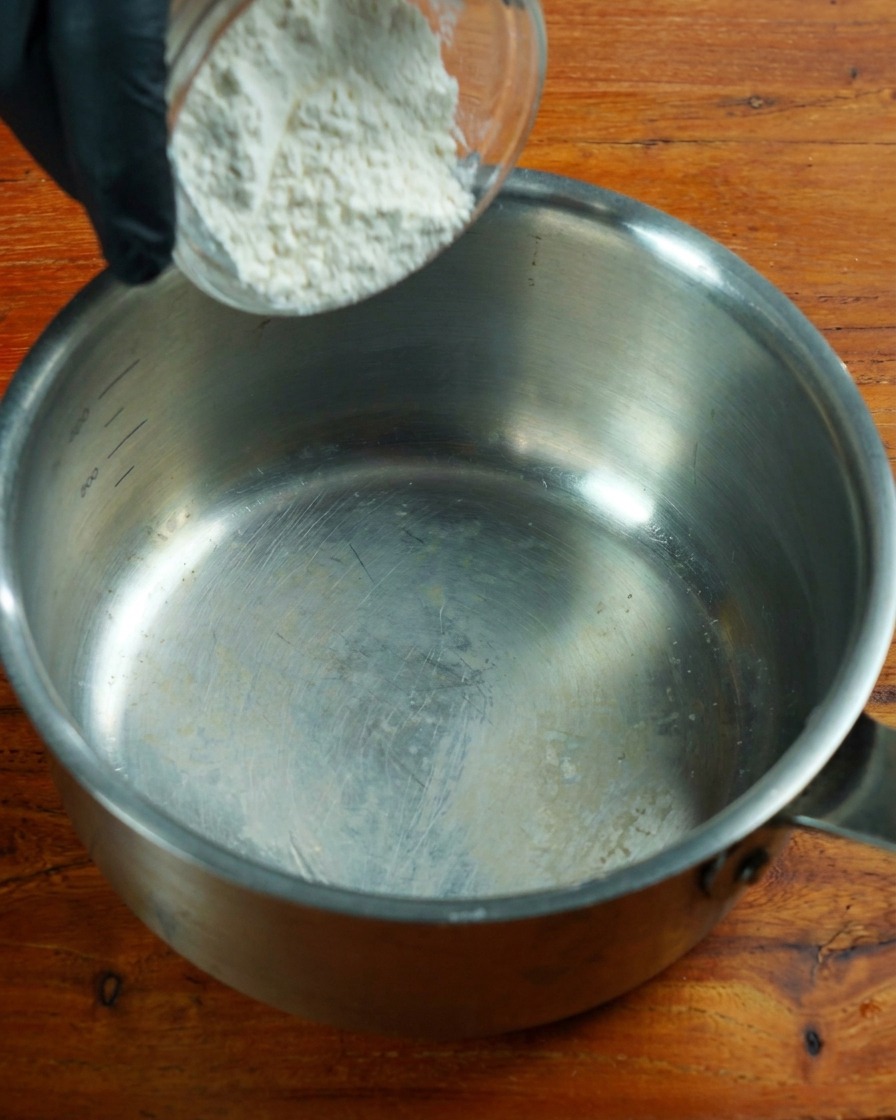 Farina povera di proteine mescolata in un pentolino dacciaio a fuoco basso.