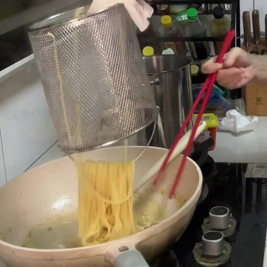 Spaghetti trasferiti nel sugo cremoso ai funghi in padella.
