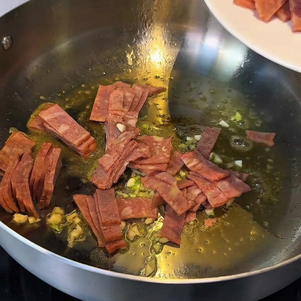Aglio e pezzetti di bacon soffritti nel burro fuso in una padella di metallo.