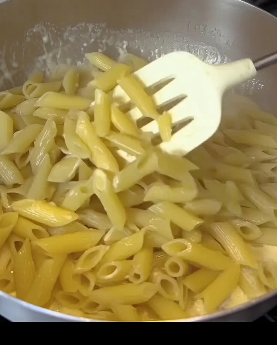 Penne mescolate in una salsa bianca cremosa con pezzi di bacon in una padella.