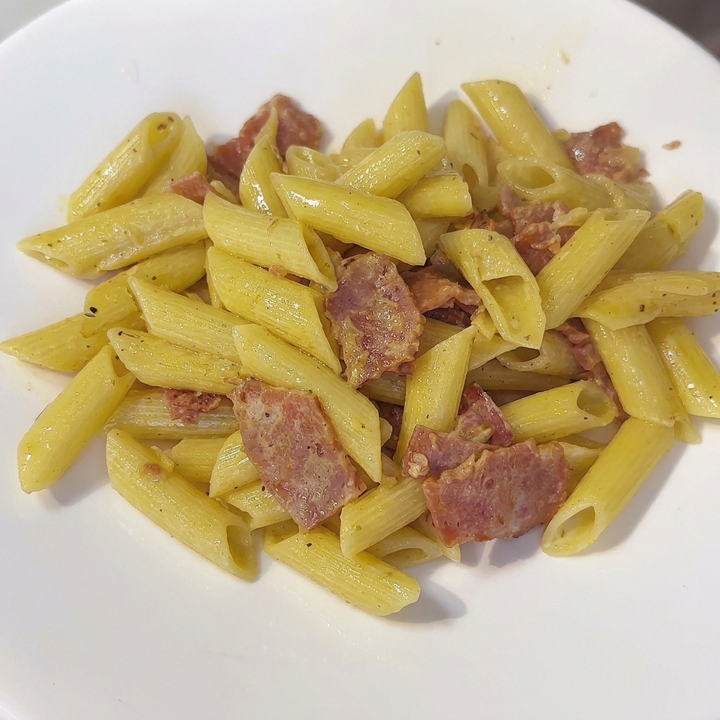 Una padella di penne cremose mescolate con una spatola.