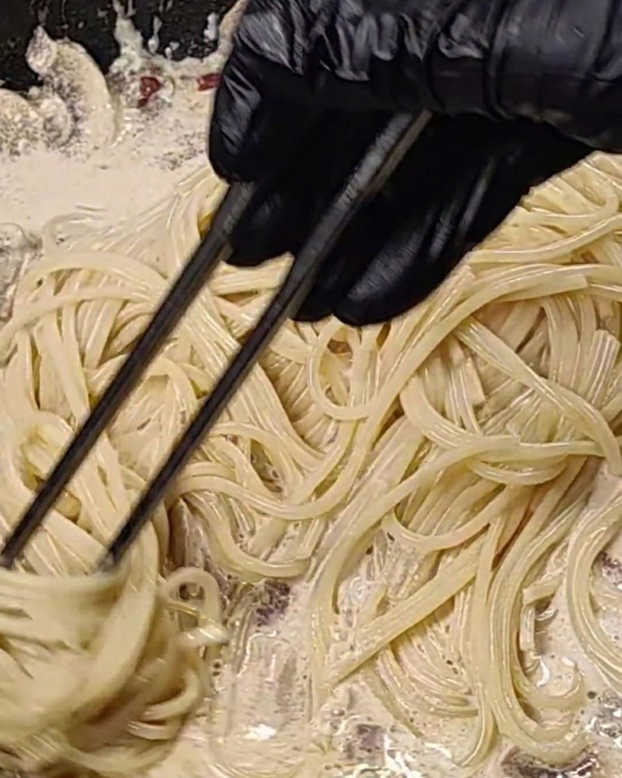 Spaghetti saltati nella salsa cremosa di pancetta e funghi in padella.