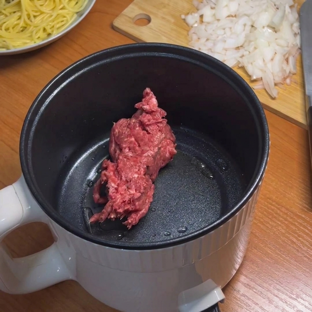 Carne macinata rosolata in una pentola elettrica con una spatola in silicone.