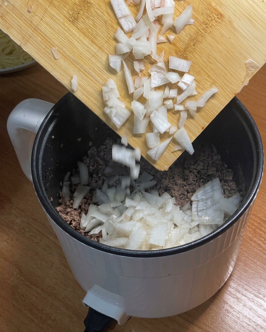 Cipolle tritate aggiunte alla carne macinata rosolata nella pentola.