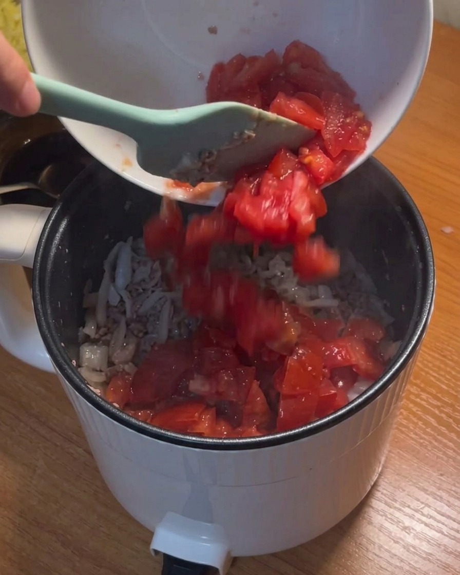Pomodori a cubetti versati in una pentola con carne e cipolle.