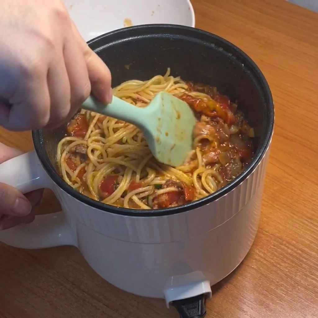 Spaghetti mescolati e ricoperti dal denso sugo rosso di pomodoro e carne.