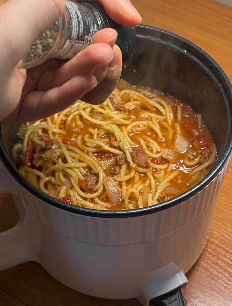 Primo piano di una pentola di spaghetti pronti, guarniti con pepe nero fresco.