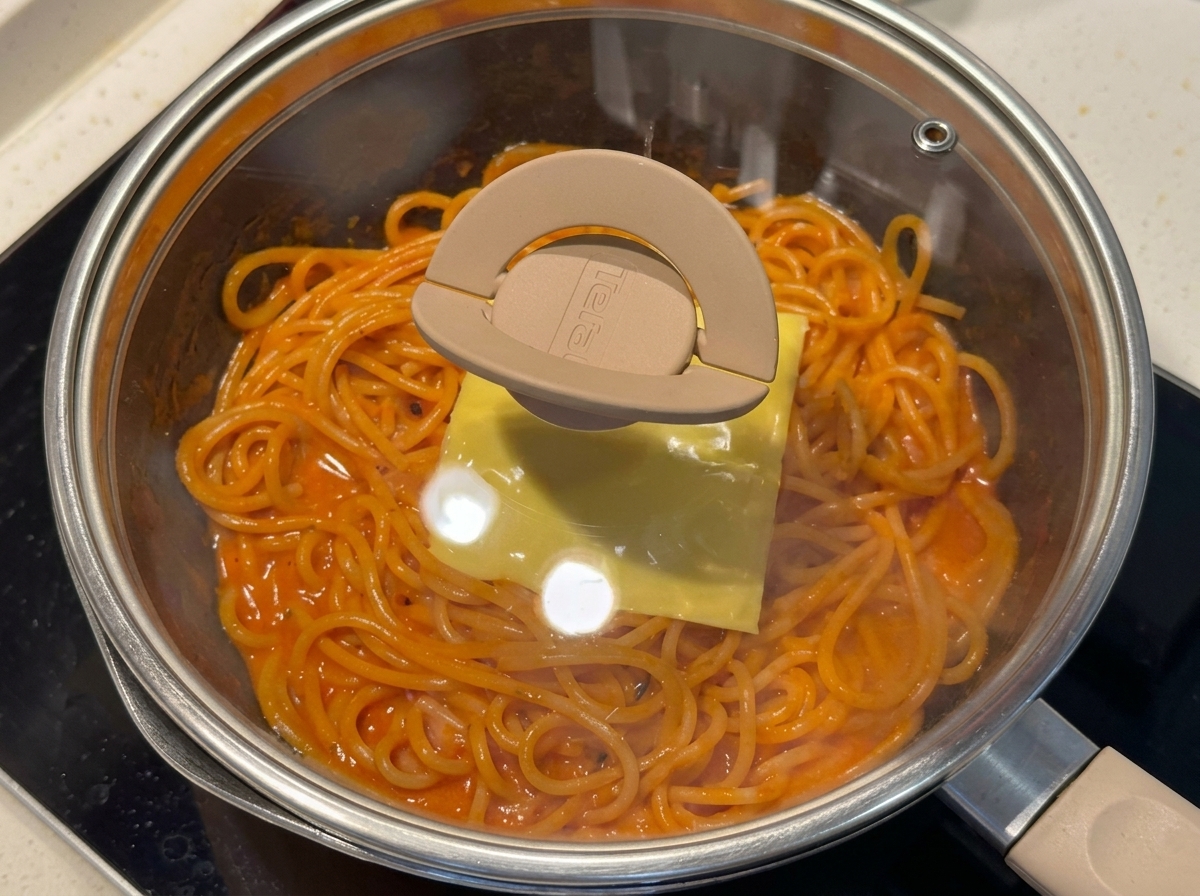 Padella con spaghetti e formaggio coperta da un coperchio di vetro.