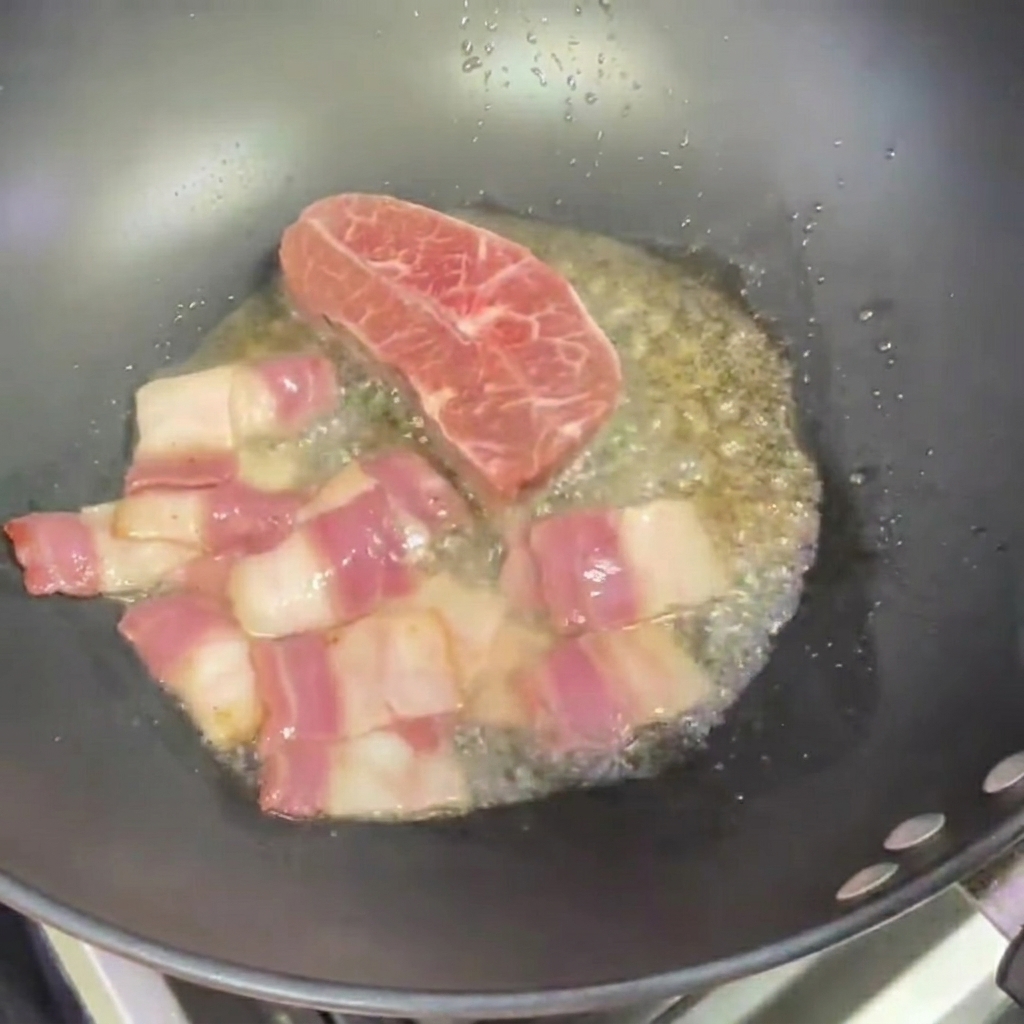 Due piccole bistecche che cuociono in un wok accanto a pezzi di bacon.