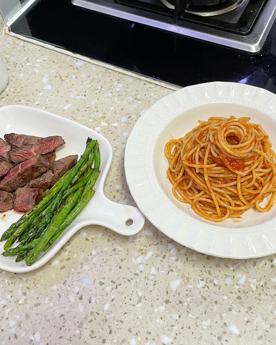 Spaghetti ben conditi sollevati da un wok con le pinze per essere impiattati in una ciotola bianca.