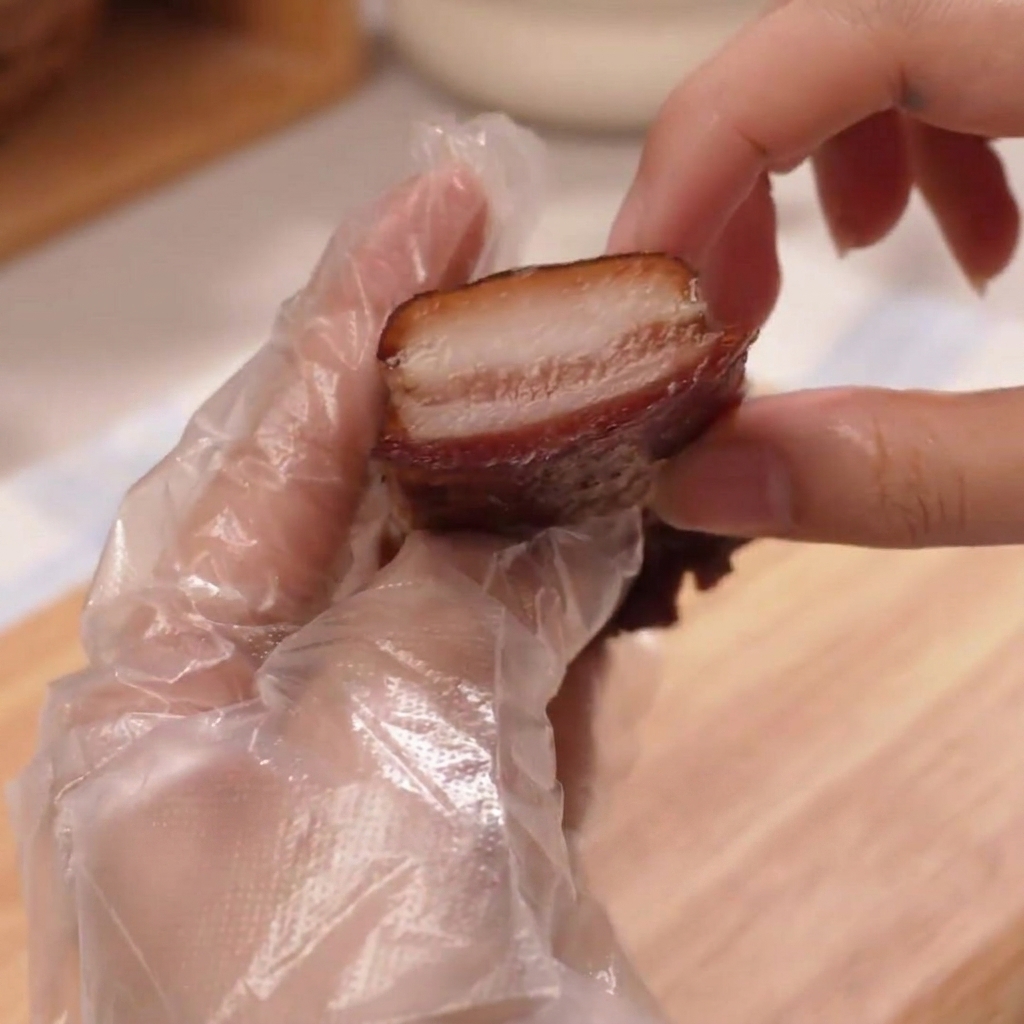 Una mano guantata che tiene una fetta di prosciutto.