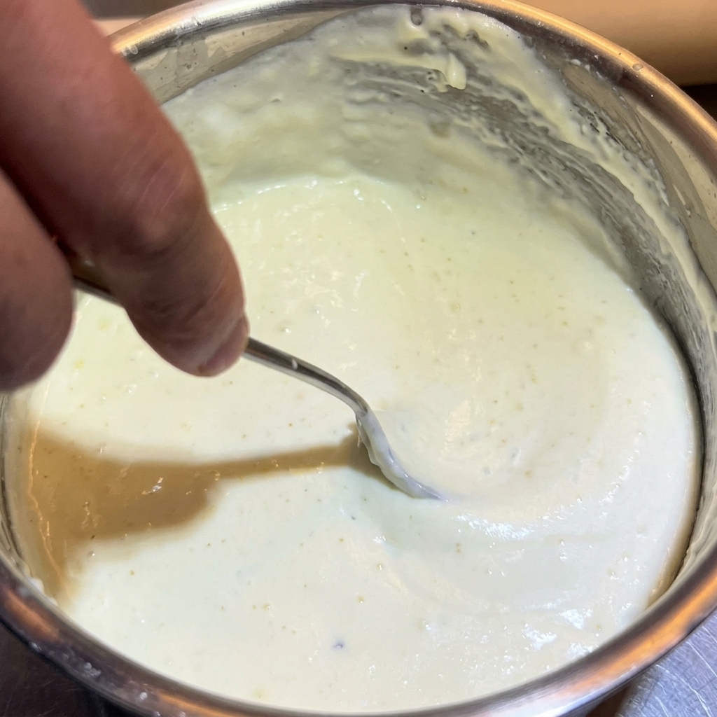 Un cucchiaio di metallo che mescola una densa salsa al formaggio.