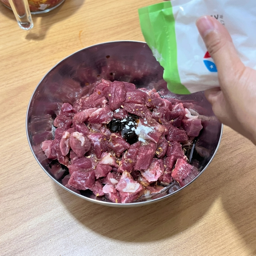 I cubetti di manzo vengono mescolati accuratamente con i condimenti liquidi e le spezie nella ciotola.
