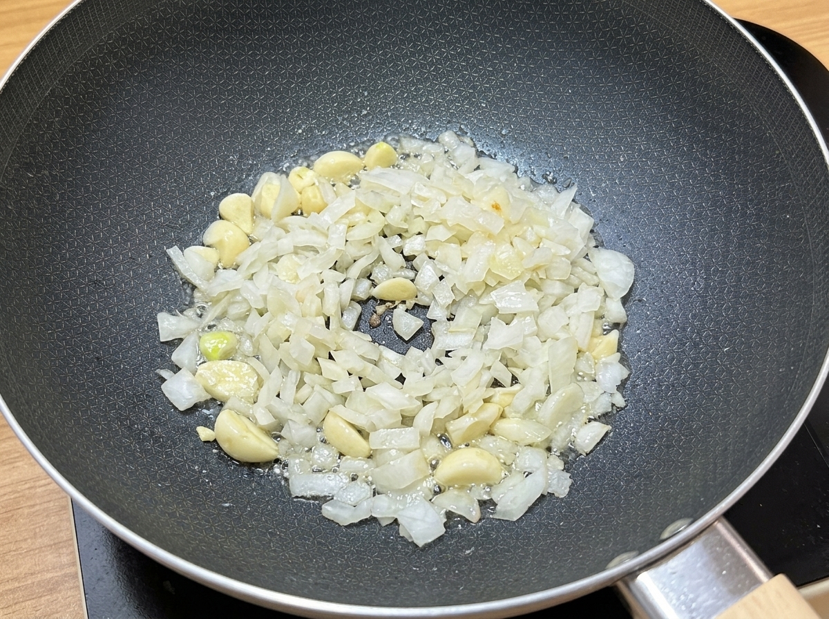 Aglio tritato e cipolle a cubetti che sfrigolano nellolio di cottura dentro una padella scura.