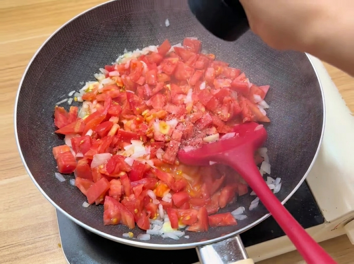 Pomodori a cubetti che cuociono in una padella con laggiunta di condimenti.