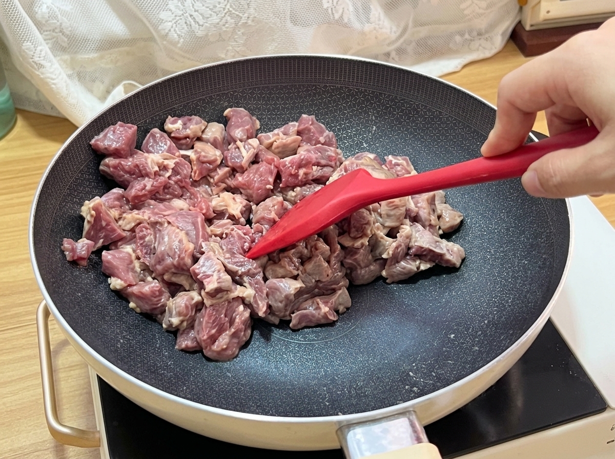 I cubetti di manzo che sfrigolano nella padella, mostrando una superficie ben rosolata.