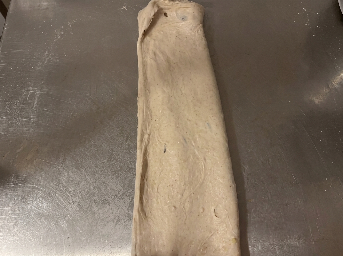 Impasto crudo ripiegato in una forma rettangolare ordinata sul piano di lavoro in acciaio.