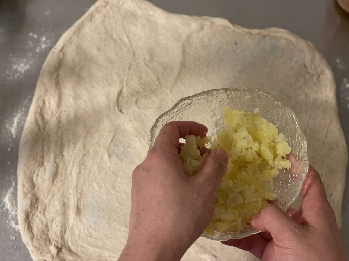 Patate a dadini e cheddar grattugiato sparsi su un foglio di impasto crudo.