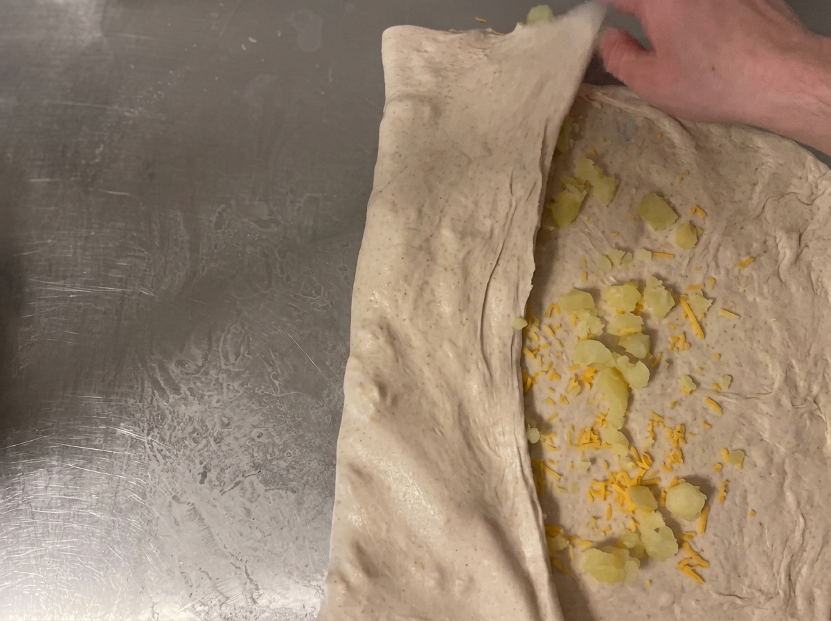 Impasto arrotolato sul piano di lavoro per sigillare il ripieno di formaggio e patate.