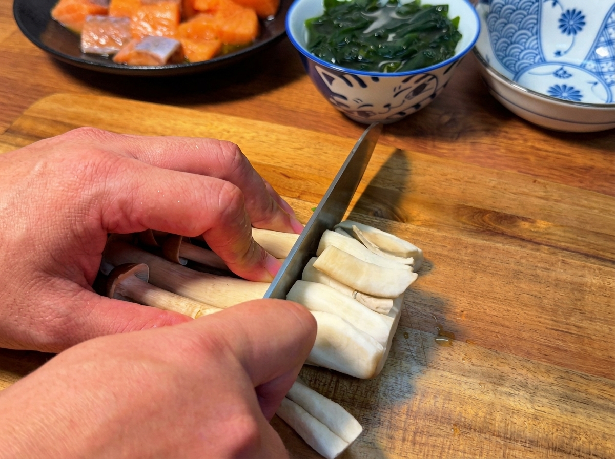 Primo piano di un coltello che taglia le basi di un mazzo di funghi shimeji su un tagliere.