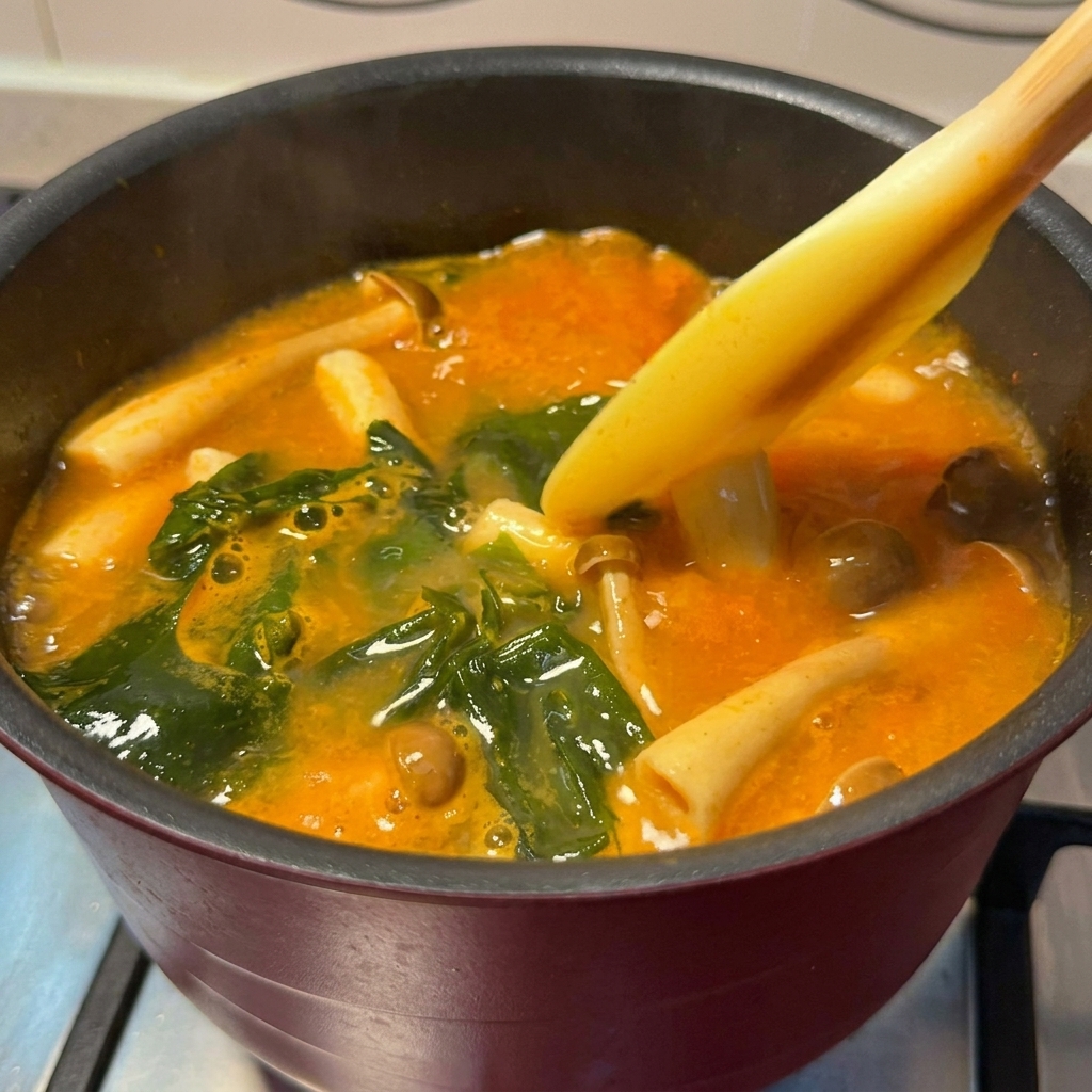 Cubetti di salmone dorati aggiunti in una pentola di zuppa piccante al miso che sobbolle.