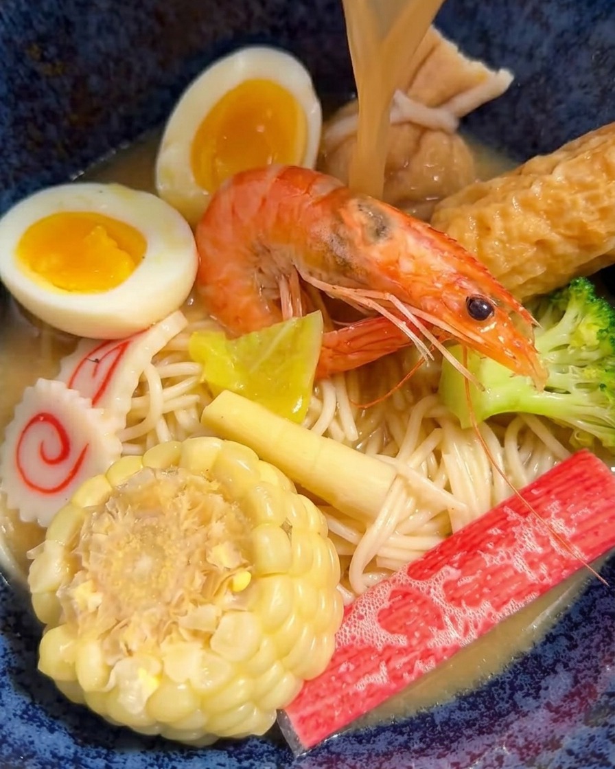 Brodo caldo al miso versato da un mestolo in una ciotola di ramen piena di vari tipi di carne e verdure.