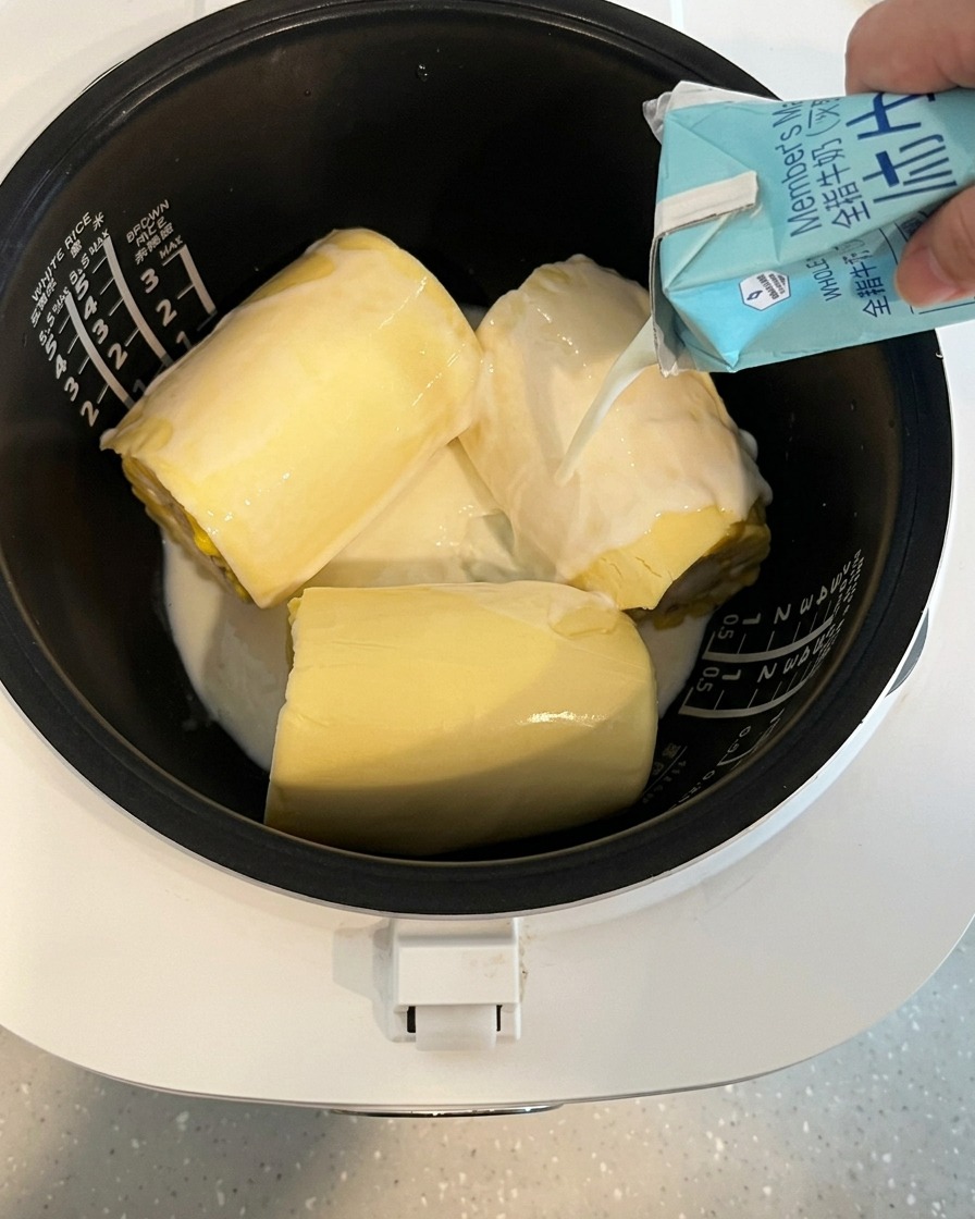 Latte versato da un cartone nella pentola del cuociriso contenente mais e formaggio.