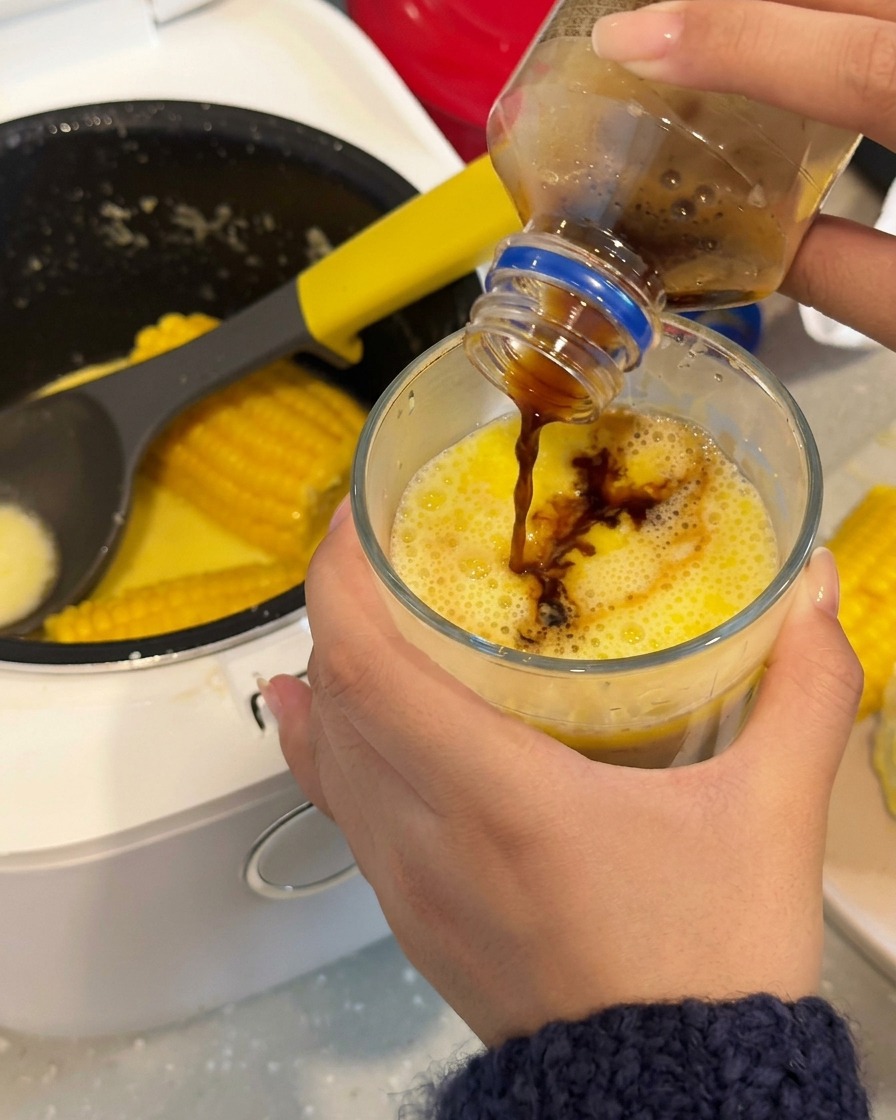 Caffè scuro versato in un bicchiere contenente un brodo di mais lattiginoso giallo brillante.
