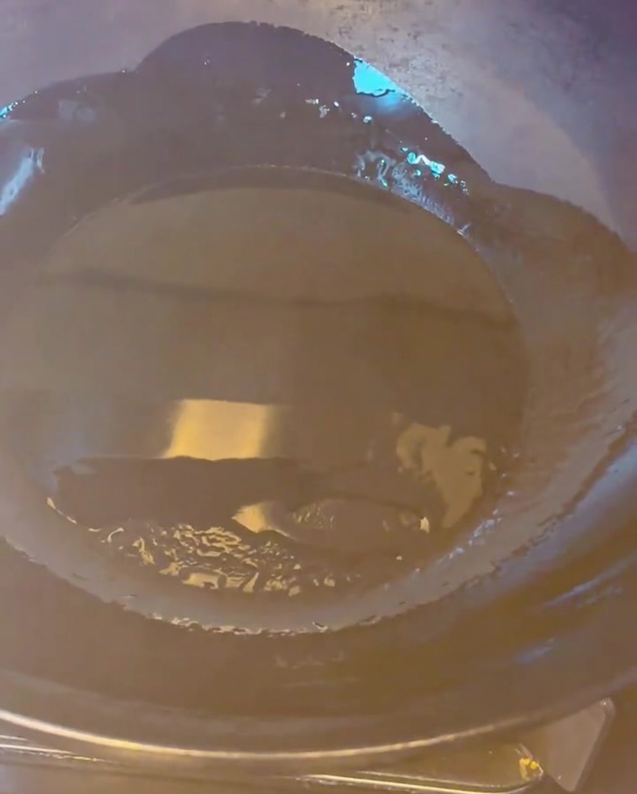 Pezzi di pancetta di maiale dorati che friggono in un wok caldo con olio.
