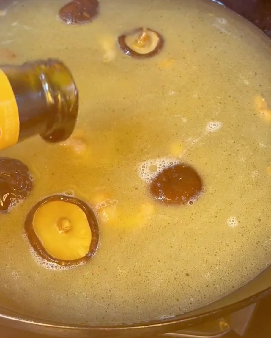 Salsa di ostriche versata da una bottiglia in un brodo dorato e bollente pieno di funghi shiitake.