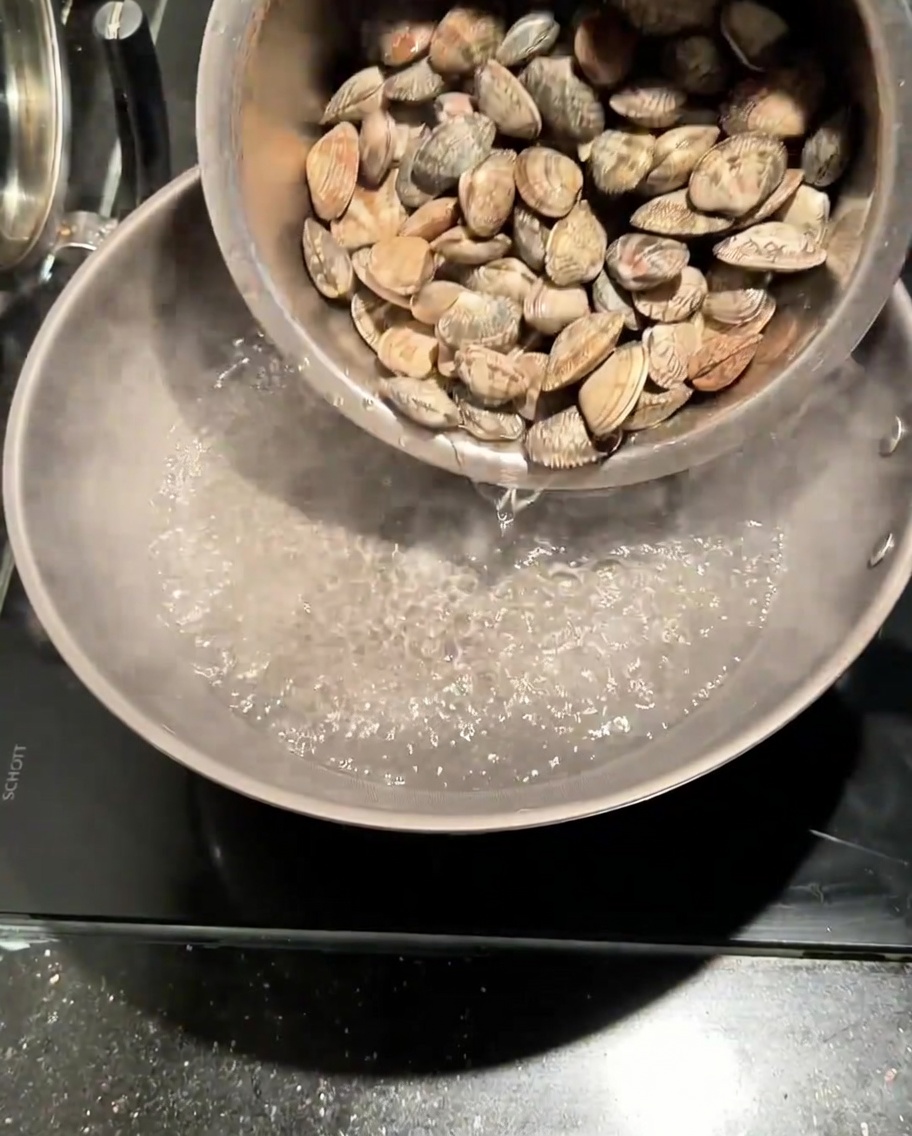 Vongole fresche versate in una pentola di acqua bollente salata.