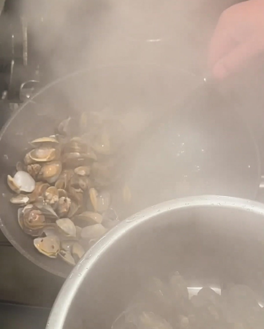 Scolapasta che preleva le vongole aperte dalla pentola bollente.