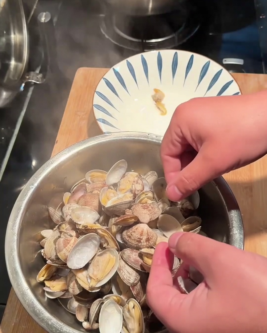 Mani che rimuovono la polpa delle vongole cotte dai gusci mettendola in una ciotola.