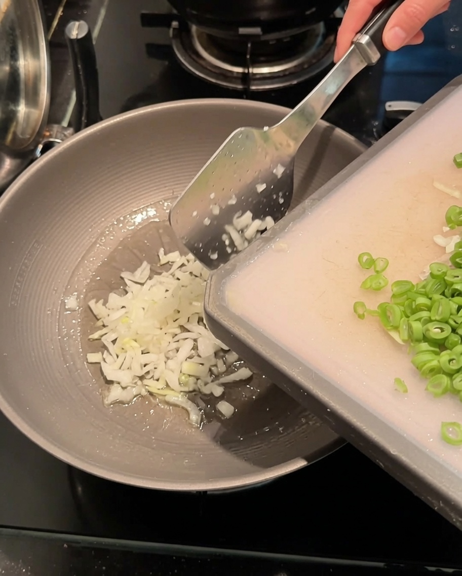 Cipollotti tritati e fagiolini a pezzetti saltati in un wok caldo con olio.