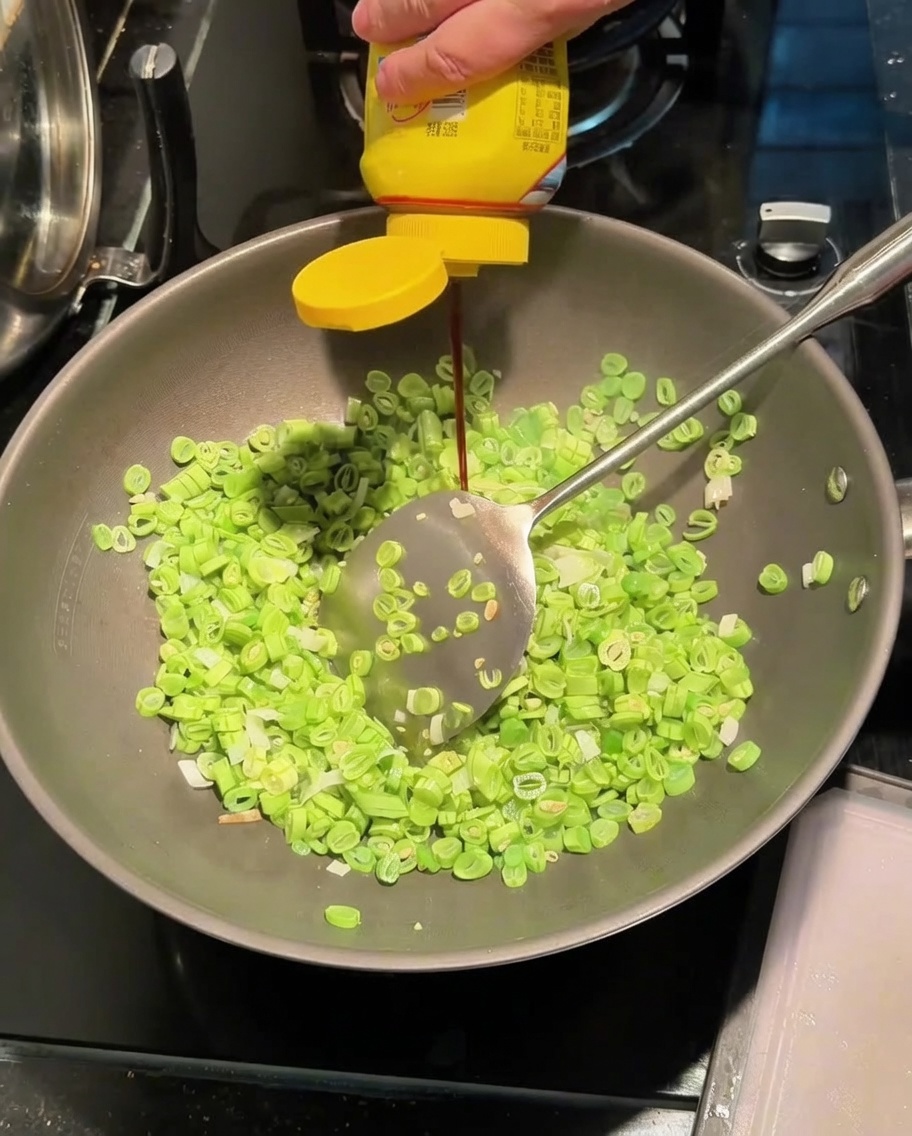 Aggiunta della salsa di condimento nel wok con fagiolini e cipollotti.