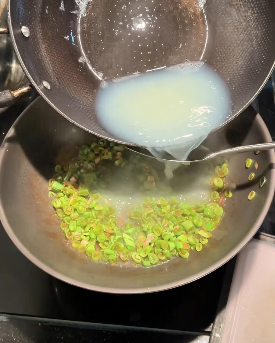 Versamento del brodo bianco di vongole dalla pentola nel wok con i fagiolini.