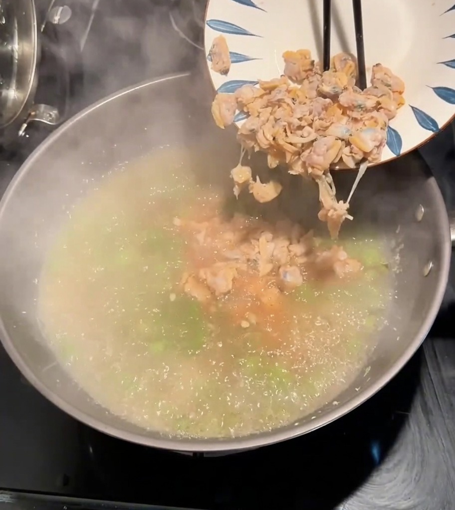 Polpa di vongole versata da un piatto nella pentola con il brodo bollente e le verdure.